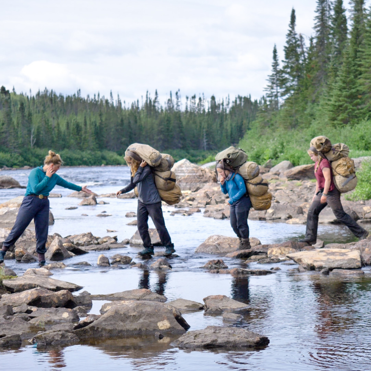 4 women walking across a river via stepping stones