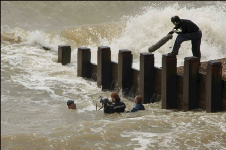 Group of people in sea in wetsuits and using camera near sea shore