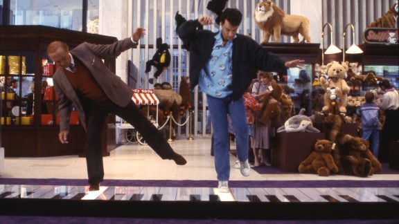 Two men jumping on large floor piano in toyshop
