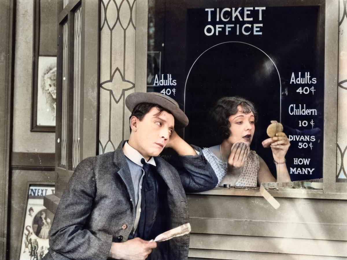 Man standing outside cinema ticket booth with woman inside doing makeup