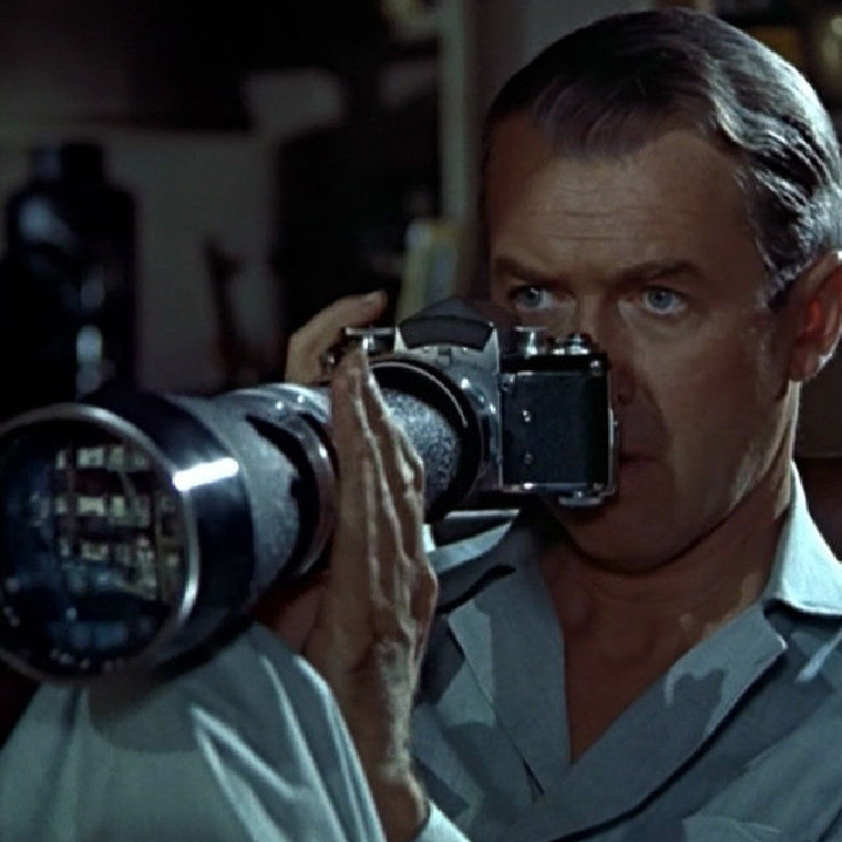 A man looking out of a window with a zoom lens