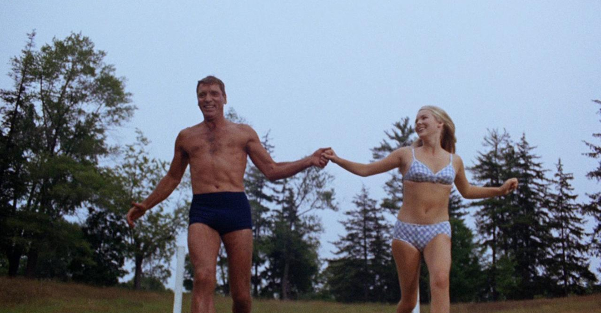 Couple laughing in swimwear jumping in to pool